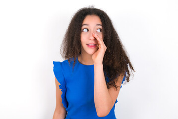 Teenager girl with afro hairstyle wearing blue T-shirt over white wall  hear incredible private...