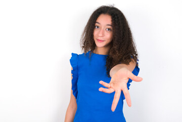 Teenager girl with afro hairstyle wearing blue T-shirt over white wall  smiling cheerful offering palm hand giving assistance and acceptance.