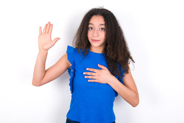Teenager girl with afro hairstyle wearing blue T-shirt over white wall  Swearing with hand on chest and open palm, making a loyalty promise oath - obrazy, fototapety, plakaty