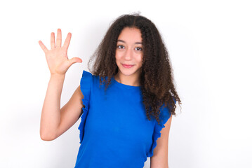 Teenager girl with afro hairstyle wearing blue T-shirt over white wall  showing and pointing up with fingers number five while smiling confident and happy.