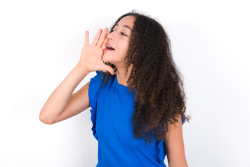 Teenager girl with afro hairstyle wearing blue T-shirt over white wall  shouting and screaming loud to side with hand on mouth. Communication concept.