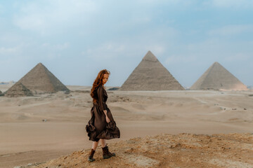 Young redhead tourist girl wearing a brown dress standing on the sand in Egypt, Cairo - Giza....