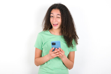 Teenager girl with afro hairstyle wearing green T-shirt over white wall taking a selfie  celebrating success