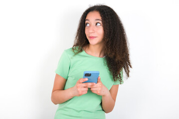 Teenager girl with afro hairstyle wearing green T-shirt over white wall holds telephone hands reads good youth news look empty space advert