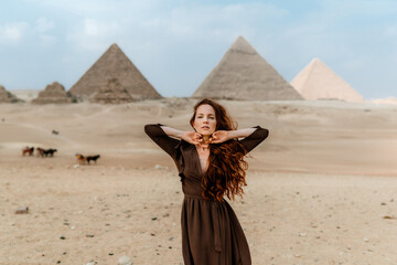 Young redhead tourist girl wearing a brown dress standing on the sand in Egypt, Cairo - Giza....