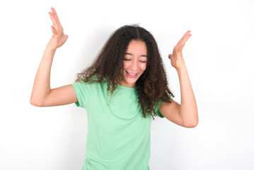 Teenager girl with afro hairstyle wearing green T-shirt over white wall goes crazy as head goes around feels stressed because of horrible situation