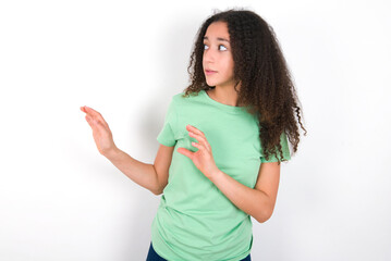 Displeased Teenager girl with afro hairstyle wearing green T-shirt over white wall keeps hands towards empty space and asks not come closer sees something unpleasant