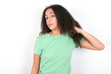 Teenager girl with afro hairstyle wearing green T-shirt over white wall stressed, anxious, tired and frustrated, pulling shirt neck, looking frustrated with problem