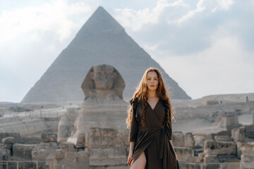 Young redhead woman standing in front of the Great Sphinx of Giza with the amazing Pyramid at the...