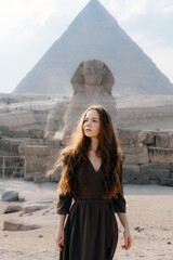 Young redhead woman standing in front of the Great Sphinx of Giza with the amazing Pyramid at the back. Valley of the Kings, Cairo, Egypt.