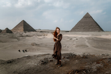 Young redhead tourist girl wearing a brown dress standing on the sand in Egypt, Cairo - Giza....