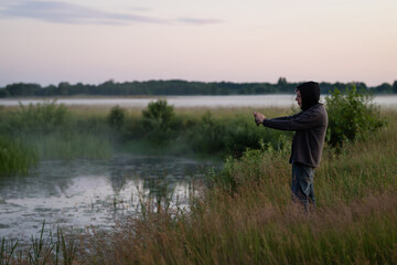 Naklejka na ściany i meble A mature man shoots an evening landscape using a smartphone. Side view