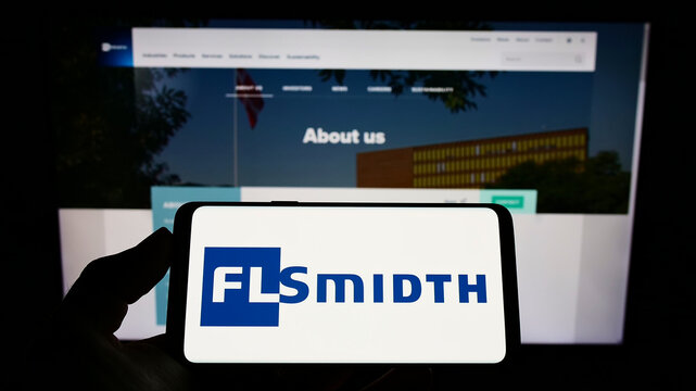 Stuttgart, Germany - 01-30-2022: Person holding mobile phone with logo of Danish engineering FLSmidth Co. AS on screen in front of business web page. Focus on phone display.