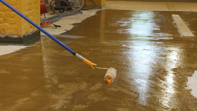 The process of applying a primer with a roller and a spatula on a concrete floor. The process of priming the plastered surface. Concrete floor primer to strengthen the surface.