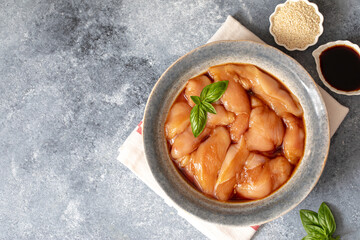 Raw diet marinated chicken meat with teriyaki sauce in a grey bowl. Marinating meat for cooking barbecue