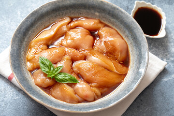 Raw diet marinated chicken meat with teriyaki sauce in a grey bowl. Marinating meat for cooking barbecue