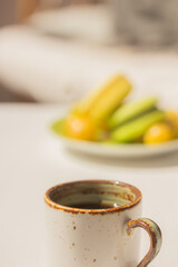 A ceramic cup of coffee or tea, a plate with  fruit snack on the table in light elegant summer interior. Summer vibes