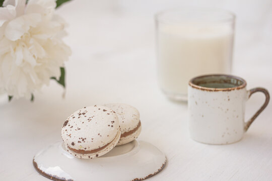 White creamy macarons, coffee or tea, white peony, candle on white background. Freshness concept. Traditional French dessert for coffee. High quality photo