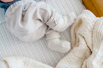 Fototapeta na wymiar Baby's legs in warm socks and pants on a white plaid