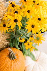 A decorative autumn front porch set up with pumpkins, gourds, mums, black eyed Susan’s, and a hay bale.