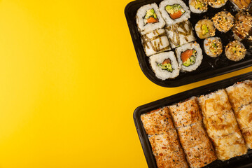 Delicious sushi rolls in disposable boxes on a yellow background. Food delivery concept. Food in the office. Japanese food. Flat lay top view, with copy space and space for text.