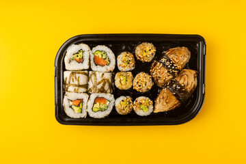 Delicious sushi rolls in disposable boxes on a yellow background. Food delivery concept. Food in the office. Japanese food. Flat lay top view, with copy space and space for text.