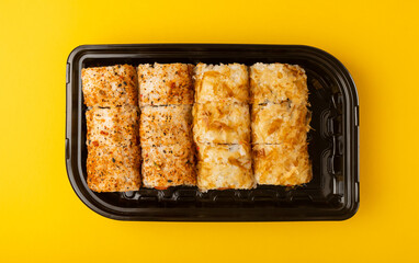 Delicious sushi rolls in disposable boxes on a yellow background. Food delivery concept. Food in the office. Japanese food. Flat lay top view, with copy space and space for text.