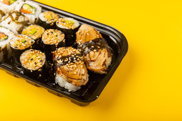 Delicious sushi rolls in disposable boxes on a yellow background. Food delivery concept. Food in the office. Japanese food. Flat lay top view, with copy space and space for text.