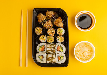 Delicious sushi rolls in disposable boxes on a yellow background. Food delivery concept. Food in the office. Japanese food. Flat lay top view, with copy space and space for text.