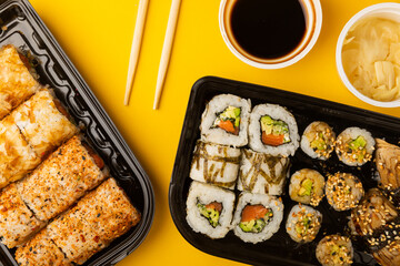 Delicious sushi rolls in disposable boxes on a yellow background. Food delivery concept. Food in the office. Japanese food. Flat lay top view, with copy space and space for text.
