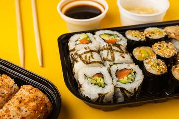 Delicious sushi rolls in disposable boxes on a yellow background. Food delivery concept. Food in the office. Japanese food. Flat lay top view, with copy space and space for text.