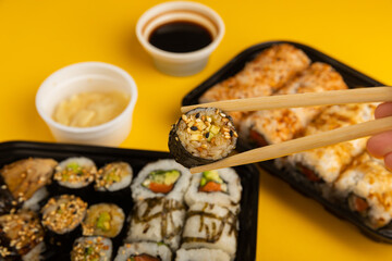 Delicious sushi rolls in disposable boxes on a yellow background. Food delivery concept. Food in the office. Japanese food. Flat lay top view, with copy space and space for text.