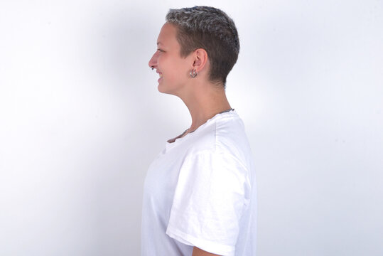 Profile of smiling young woman with short hair wearing white t-shirt over white background with healthy skin, has contemplative expression, ready to have outdoor walk.