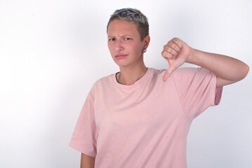 young woman with short hair wearing pink t-shirt over white background looking unhappy and angry...
