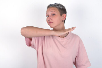 young woman with short hair wearing pink t-shirt over white background cutting throat with hand as...