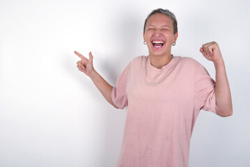 Naklejka premium Cheerful young woman with short hair wearing pink t-shirt over white background showing copy space ad celebrating luck