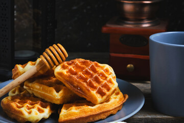 Waffles sweet pastries on plate, against background coffee grinder and decorative lamp with candle.