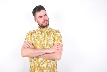 Image of upset young handsome bearded man wearing flowered shirt over white wall with arms crossed....
