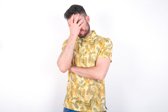 Young caucasian man wearing Hawaiian t-shirt over white background  making facepalm gesture while smiling amazed with stupid situation.