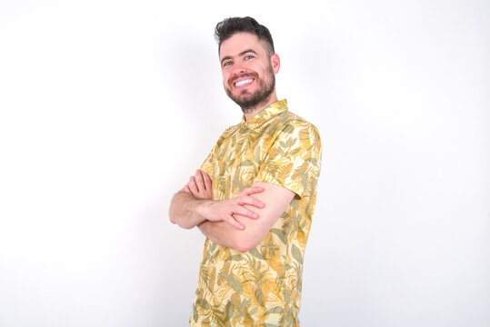 Image of cheerful Young caucasian man wearing Hawaiian t-shirt over white background  with arms crossed. Looking and smiling at the camera. Confidence concept.