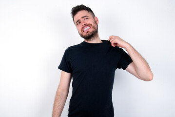 young caucasian bearded man wearing black t-shirt standing over white wall stressed, anxious, tired and frustrated, pulling shirt neck, looking frustrated with problem