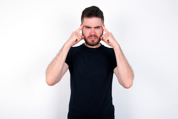 Serious concentrated young caucasian bearded man wearing black t-shirt  keeps fingers on temples, tries to ease tension, gather with thoughts and remember important information for exam