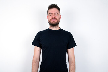 young caucasian bearded man wearing black t-shirt standing over white wall nice-looking sweet charming cute attractive lovely winsome sweet peaceful closed eyes