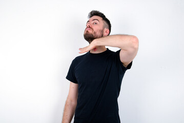 young caucasian bearded man wearing black t-shirt standing over white wall cutting throat with hand...