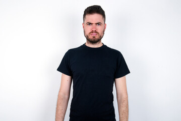 Fototapeta premium young caucasian bearded man wearing black t-shirt standing over white wall Pointing down with fingers showing advertisement, surprised face and open mouth
