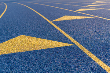 Fototapeta na wymiar Inspiring close up of the start of an exchange zone on a new blue running track with yellow lane lines and other markings.