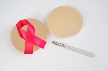 Breast silicone implants, pink tape and a disposable scalpel on a white background. 