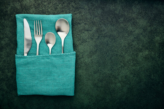 Linen Napkin Pocket With Steel Cutlery On A Dark Green Background With Copy Space