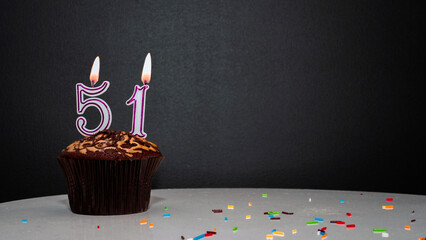 Muffin on black with a number from a candle number 51. Copy space, a pie on a black background, a...
