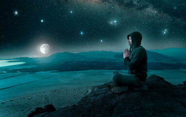 person sitting on the top of the mountain meditating or contemplating the starry night with full...